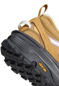 Gros plan d'une chaussure marron et beige avec une semelle extérieure Vibram noire et une boucle blanche à la cheville.