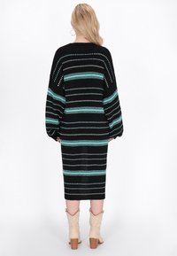 Musta neulemekko vaakasuorilla turkoosi- ja valkoviiruilla, jossa on pitkät hihat ja tiukka siluetti, yhdistettynä beigekiilakorkoisiin nilkkureihin.