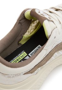 Sneaker multi-material in beige e marrone con un design testurizzato, fodera in tessuto morbido e un'etichetta prominente con codice QR e branding.