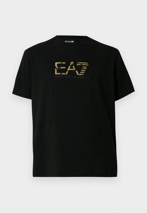 Crna majica kratkih rukava s zlatnim EA7 Emporio Armani logotipom u sredini prsa na jednostavnoj bijeloj pozadini.