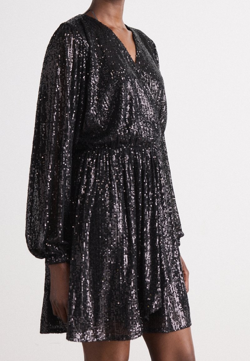 Robe courte noire à manches longues et col en V, couverte de sequins brillants, avec une taille froncée et une jupe ample et fluide.