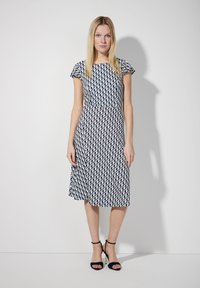 Navyblaues und weißes gemustertes Kleid mit kurzen Ärmeln, tailliertem Schnitt und weit schwingendem Rock. Getragen mit schwarzen, geschnallten High Heels.