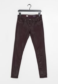 Jeans slim fit marrone scuro appesi a un gancio nero su uno sfondo bianco, che mostrano le tasche anteriori e la chiusura con bottone.