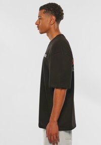 Sort bomulds T-shirt med korte ærmer, afslappet pasform, med grafiske prints foran og bagpå. Båret med lyse denimbukser.