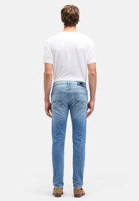 Jasnoniebieskie dżinsy o prostych nogawkach z delikatnym wyblaknięciem, posiadające dwie tylne kieszenie i subtelne detale szwów, noszone z prostą białą koszulką.
