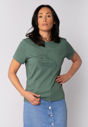 Groene katoenen t-shirt met korte mouwen, voorzien van een zwarte lijntekening van handen en bladeren. Gecombineerd met een lichte denim rok.