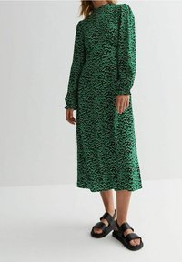 Vihreä midi-mekko pitkillä hihoilla, tekstuuripainokuvio, ja mustat tukevat sandaalit leveillä remmeillä ja paksulla pohjalla.