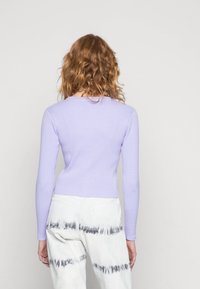 Vaaleanlaventelinsävyinen ribbineulottu pitkähiha neule, yhdistettynä valkoisiin housuihin, joissa on harmaa pilkullinen kuvio lahkeen alareunassa. Pehmeä materiaali, istuva malli.