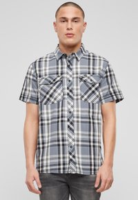 Košeľa s krátkym rukávom, károvaná v modrej, čiernej a bielej farbe, s dvoma vreckami na hrudi, zapínaním na gombíky a voľným strihom.