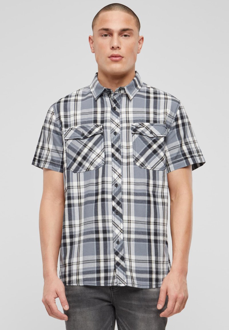 Košeľa s krátkym rukávom, károvaná v modrej, čiernej a bielej farbe, s dvoma vreckami na hrudi, zapínaním na gombíky a voľným strihom.