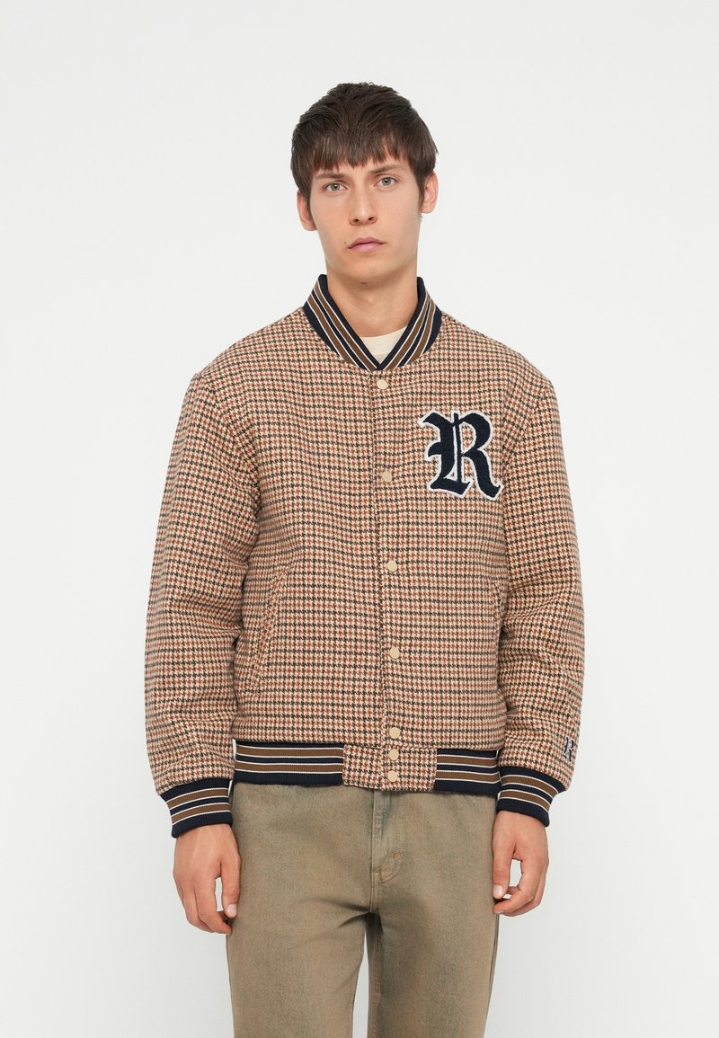 Brun houndstooth bomberjakke med marineblå ribbestrikket krage og mansjetter, med et fremtredende "R"-logo og trykknap-lukking.