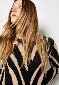 Schwarzer und beiger Pullover mit Zickzackmuster, gestrickte Textur, Rundhalsausschnitt, lange Ärmel, mit kontrastierenden Farben und einer taillierten Passform.