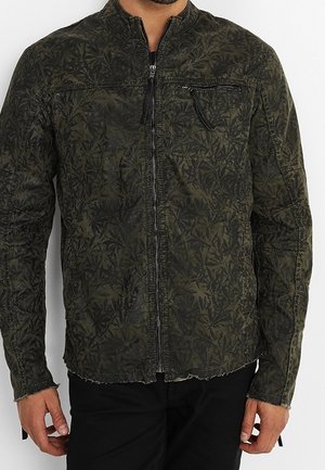Giacca zip-up verde oliva con motivo a foglia, dotata di colletto rialzato e una tasca sul petto con chiusura a zip. Tessuto strutturato con bordi grezzi.