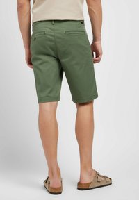 Gröna bomullsshorts med rak skärning, med bakfickor och en knappdetalj. Bärs med bruna sandaletter och en ljus skjorta.