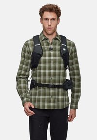 Groen en witte geruite shirt met lange mouwen, gedragen met een zwarte, verstelbare harnas met opbergvakken en gespen.