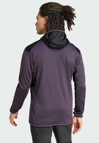 Felpa viola con cappuccio nero e accenti sulle spalle. Tessuto texture, maniche lunghe e orlo posteriore leggermente allungato.