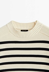 Pull en tricot rayé crème et noir avec un col rond côtelé et un tissu texturé ; présente de larges rayures horizontales et des détails subtils.