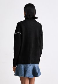 Svart stickad tröja med hög halsringning, ribbade ärmslut och vit accenttråd, tillsammans med en utsvängd denimkjol.