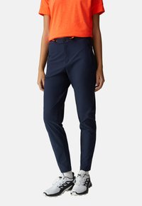 Pantalon bleu marine fuselé avec poches zippées, taille élastique et cordon de serrage orange, assorti à des baskets blanches et des chaussettes mi-mollet.