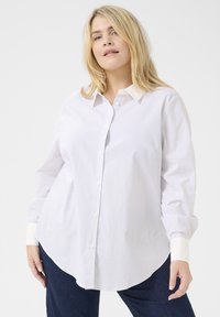 Camisa de botones a rayas blancas y azules claras con cuello clásico, mangas largas y dobladillo redondeado. Tejido suave, puños blancos en contraste.