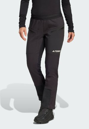 Black outdoor pants with zippered pockets and reinforced lower panels. Made from durable, stretchy fabric, designed for mobility and comfort.