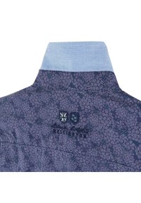 Col de chemise à motifs marine avec doublure intérieure bleu clair, présentant des motifs floraux et un détail de blason brodé.