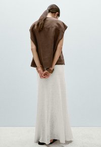 Bruine suède top met korte mouwen, gecombineerd met een lange witte textuurskirt. Accessoires zijn houten armbanden om de polsen.