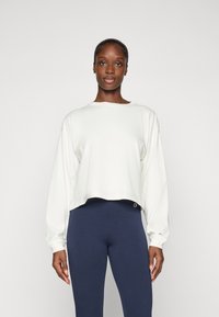 Hvit cropped hettegenser med lange ermer og en subtil logo. Sammen med marineblå leggings med et merkelapp på midjebåndet.
