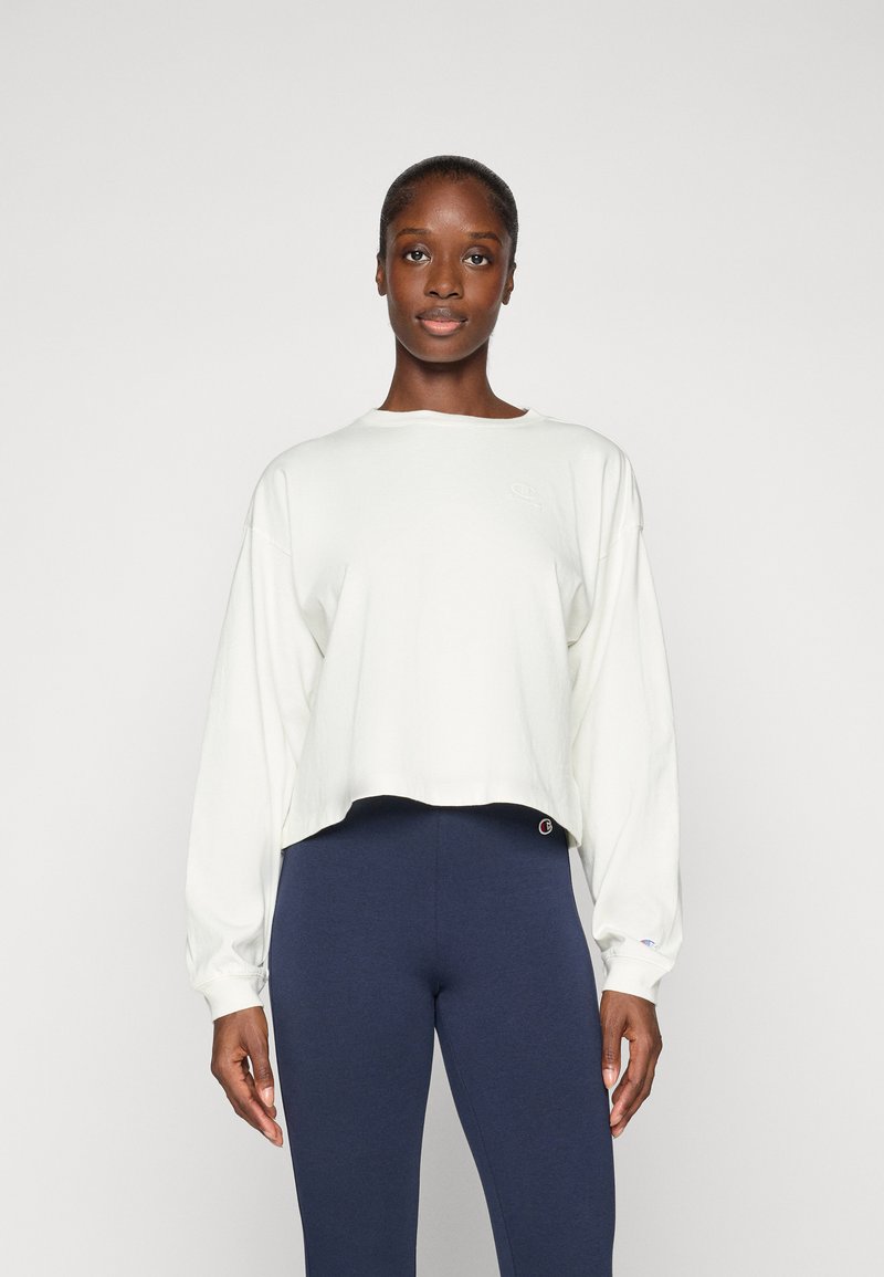 Hvit cropped hettegenser med lange ermer og en subtil logo. Sammen med marineblå leggings med et merkelapp på midjebåndet.