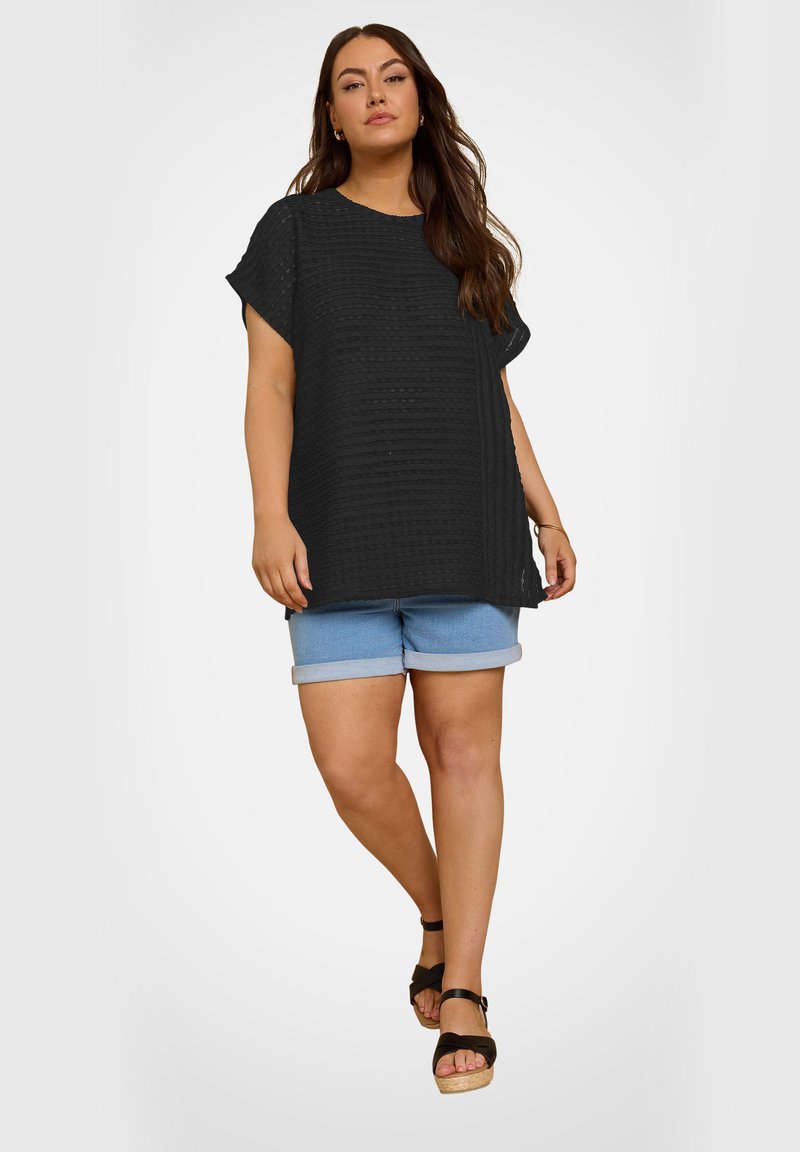 Black textured oversized top with short sleeves, paired with light blue denim shorts featuring rolled cuffs and black platform sandals.