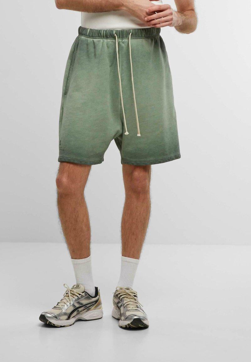 Shorts en sweat à dégradé vert avec une taille élastique et un cordon de serrage, dotés de poches latérales et d'une texture de tissu douce.