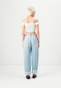 Bela off-the-shoulder kratka majica s valovitim rubom, uparena s svijetloplavim trapericama visokog struka koje imaju širok kroj i sužene gležnjeve.