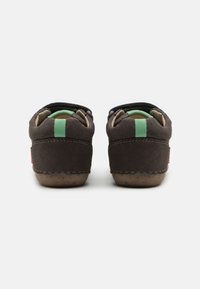 Zapatos de ante marrón con una franja de acento verde en la parte trasera, forro interior suave y suela de goma texturizada. Presenta dos aberturas laterales.