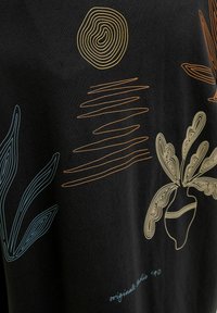 T-shirt noir avec un design en ligne orange et teal. Comprend un soleil abstrait, des lignes horizontales et des motifs de plantes. Le texte indique "originals '90."