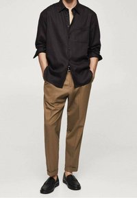 Chemise noire à manches courtes, associée à un pantalon marron clair et des mocassins noirs, présentant une coupe décontractée et une texture de tissu lisse.