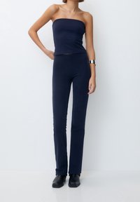 Námořnické modré top bez ramínek v kombinaci s přiléhavými námořnickými kalhotami; hladká textura; modelka má na sobě černé kotníkové boty a stříbrný náramek.