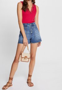 Rød ærmeløs top med blonder, høj talje denimshorts med knaplukning og en tan crossbody taske med guldfarvet hardware.