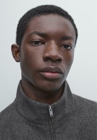 Graue Fleecejacke mit Reißverschluss und Stehkragen, mit glatter Textur und dezenten Nähdetails neben dem Reißverschluss. Einfarbiger Hintergrund.