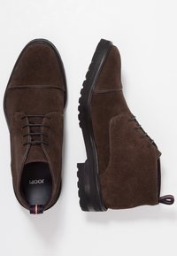 Bruine suède enkellaarzen met veters, ronde neuzen, rubberen zolen en contrasterende stiksels. Inclusief een trekband met een gestreept accent.
