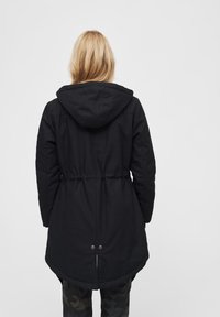 Czarna parka z kapturem, taliowana, z długim, zaokrąglonym dołem. Wykonana z trwałej tkaniny o gładkiej fakturze, bez widocznych wzorów.