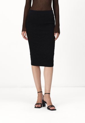 Jupe crayon noire avec un motif texturé, taille haute et longueur genou. Accordée avec des talons noirs à lanières.