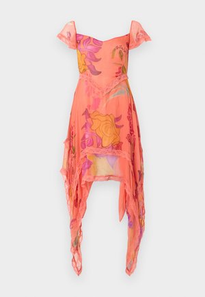 Žena nosi koralovo ružové šaty s vysokým a nízkym lemom, s čipkovou výšivkou a veľkými kvetinovými vzormi v žltej, fialovej a červenej farbe, v kombinácii s béžovými podpätkami.