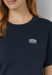 Navyblauwe katoenen t-shirt met een ronde halslijn en korte mouwen, voorzien van een geborduurd tekstdetail in wit en blauw op de borst.