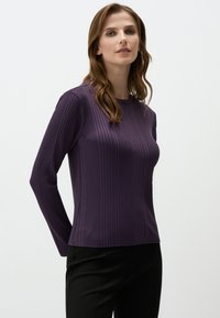 Paarse geribde langslavenshirt met een ronde hals, aansluitende pasvorm en een gladde textuur, gecombineerd met zwarte broek. Eenvoudig ontwerp en minimale details.