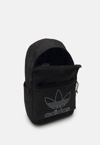 Svart stoffryggsekk med buet topp, frontlomme med glidelås, og stort blått Adidas-logo med tre bladdekorasjoner. Teksturert overflate.