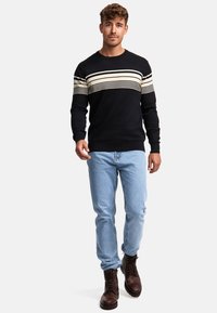 Navy-Strickpullover mit horizontalen cremefarbenen und schwarzen Streifen, kombiniert mit hellblauen Jeans und braunen Schnürstiefeln. Outfit vor einem neutralen Hintergrund gezeigt.