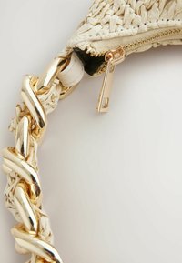 Geflochtener Strohhut mit einer dicken goldenen Kettenriemen, ausgestattet mit einem cremfarbenen Reißverschluss und einem schwarzen Innenfutter. Texturierte Oberfläche mit glänzenden Akzenten.