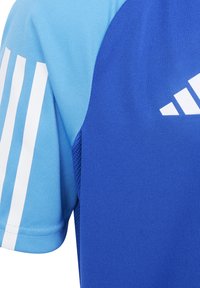 Maglietta sportiva blu con maniche azzurro chiaro e tre strisce bianche sulla manica sinistra. Include un pannello in rete per la traspirabilità.