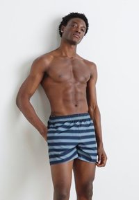 Rutet badeshorts i mørkeblå og marineblå, med elastisk linning og en avslappet passform. Glatt stoff med horisontale striper.
