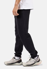 Sorte bomulds sweatpants med slim fit, der har ribbede håndled og sidelommer, parret med lysegrå løbesko og hvide sokker.